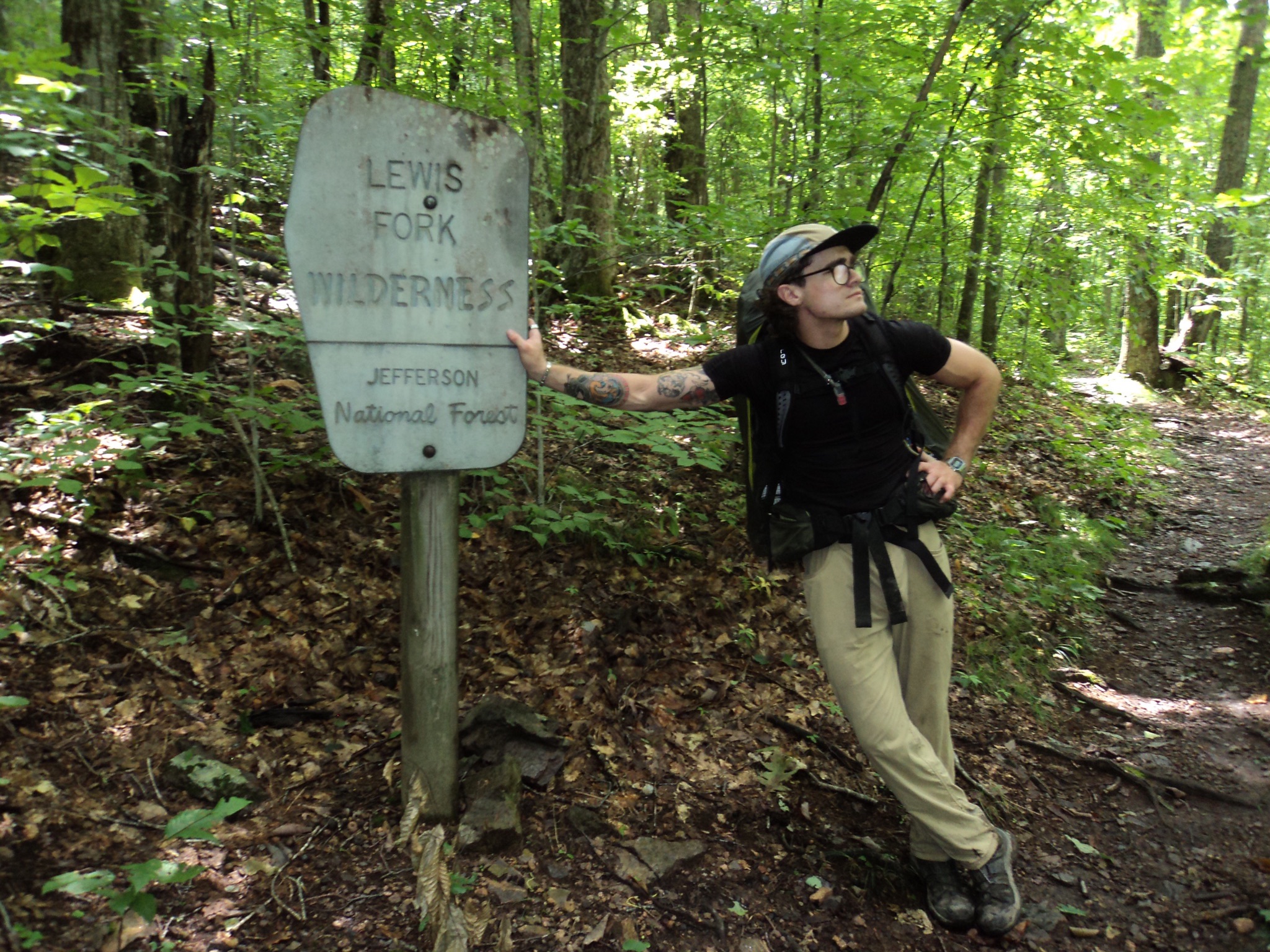Owen leaning against the Lewis Fork Wilderness trail sign in Jefferson National Forest, wearing a backpack